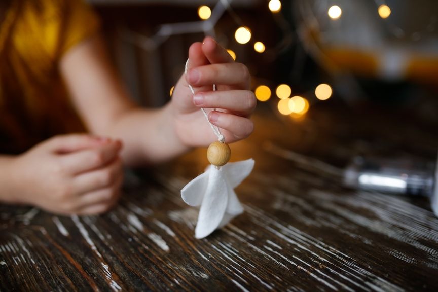 Kind hält einen schlichten Engel aus Filz mit einer Holzkugel als Kopf in der Hand