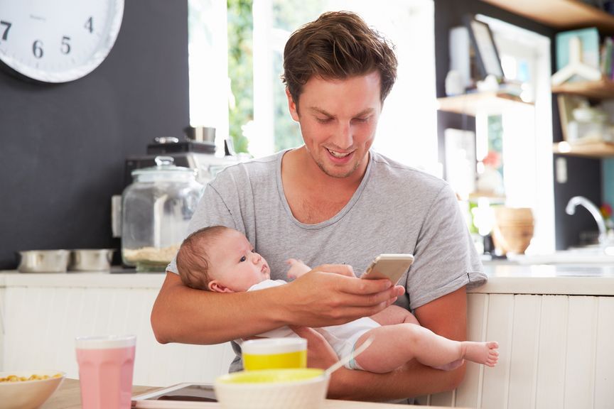 Vater mit Baby auf dem Arm schaut aufs Handy