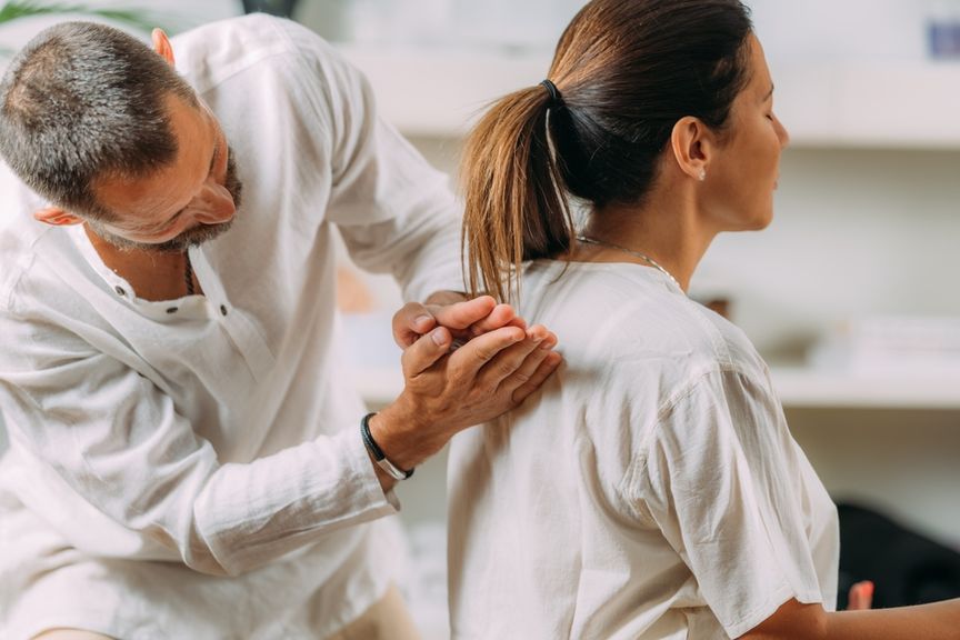 Sitzende Frau bekommt von einem Mann eine Shiatsu-Rückenmassage.