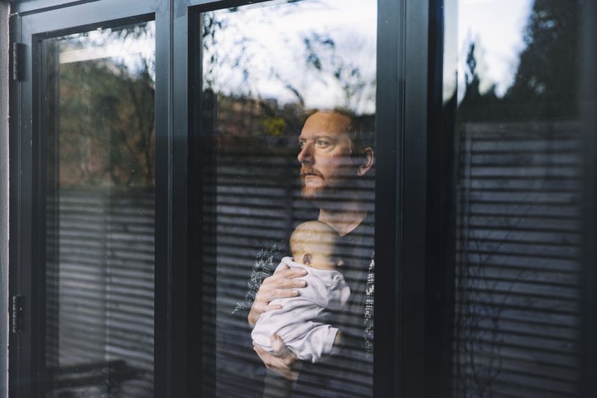 Vater mit Baby im Arm schaut nachdenklich aus dem Fenster