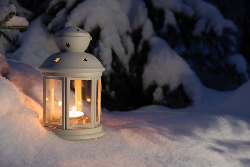 Weisse Laterne mit einem Teelicht steht in der Dunkelheit im Schnee