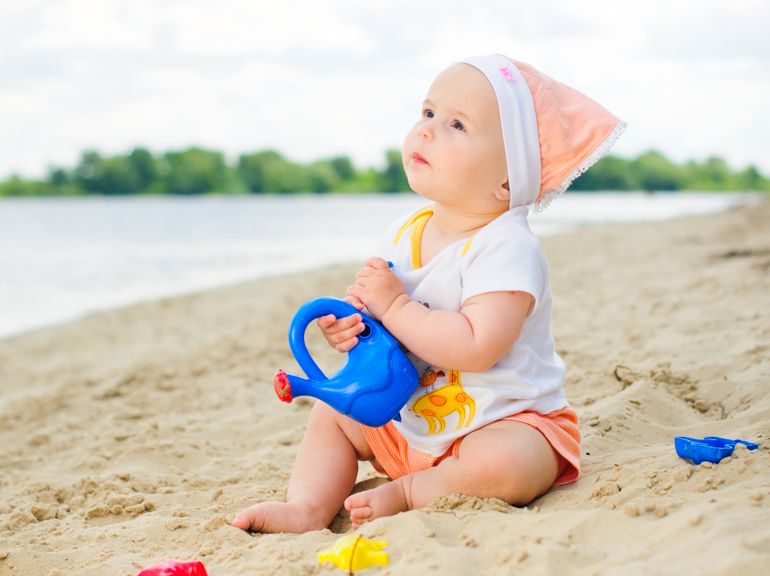 Baby mit Spielzeug am Strand