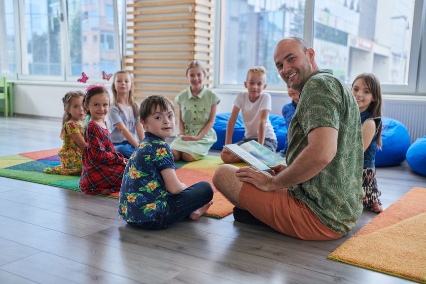 Mann liest einer Kindergruppe, die im Kreis sitzt, aus einem Buch vor