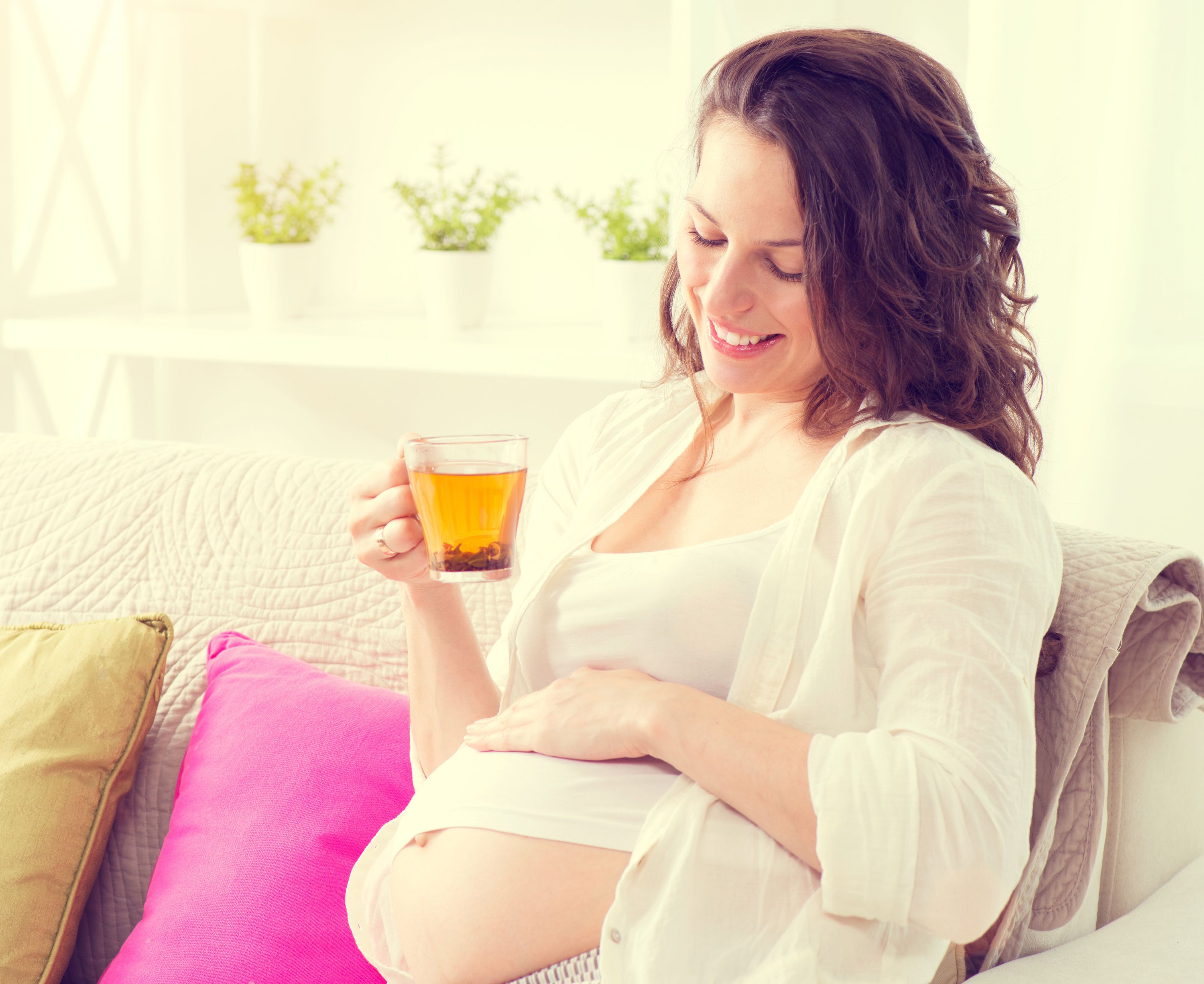 Schwangere sitzt auf dem Sofa und trinkt eine Tasse Tee
