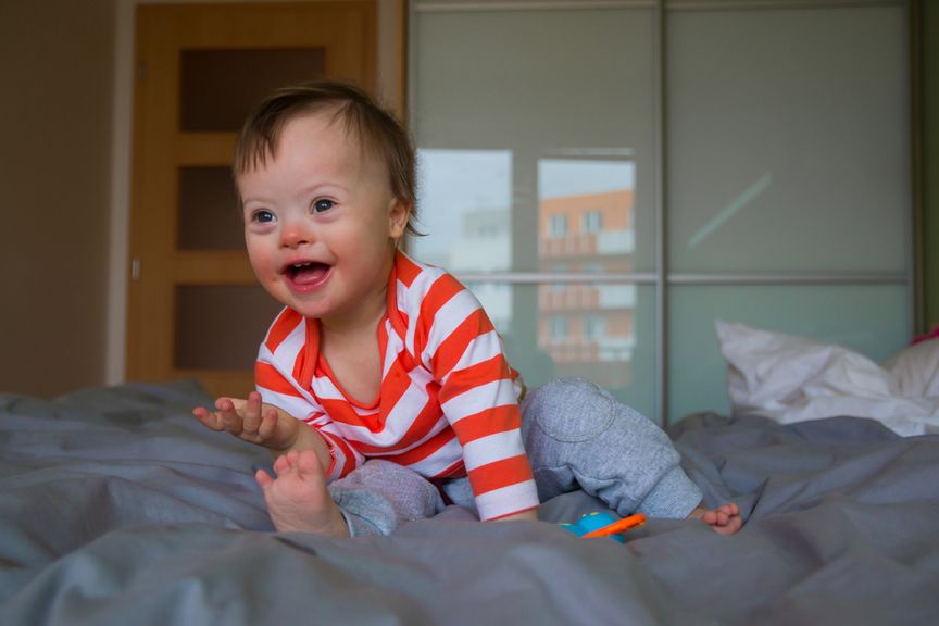 Lachendes Kind mit Down Syndrom spielt auf dem Elternbett
