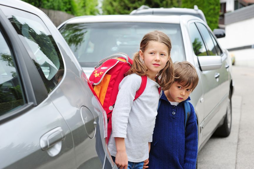 Schulkinder auf der Strasse zwischen parierten Autos