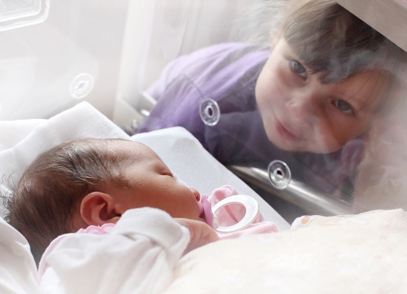 Geschwister schaut ins Babybett