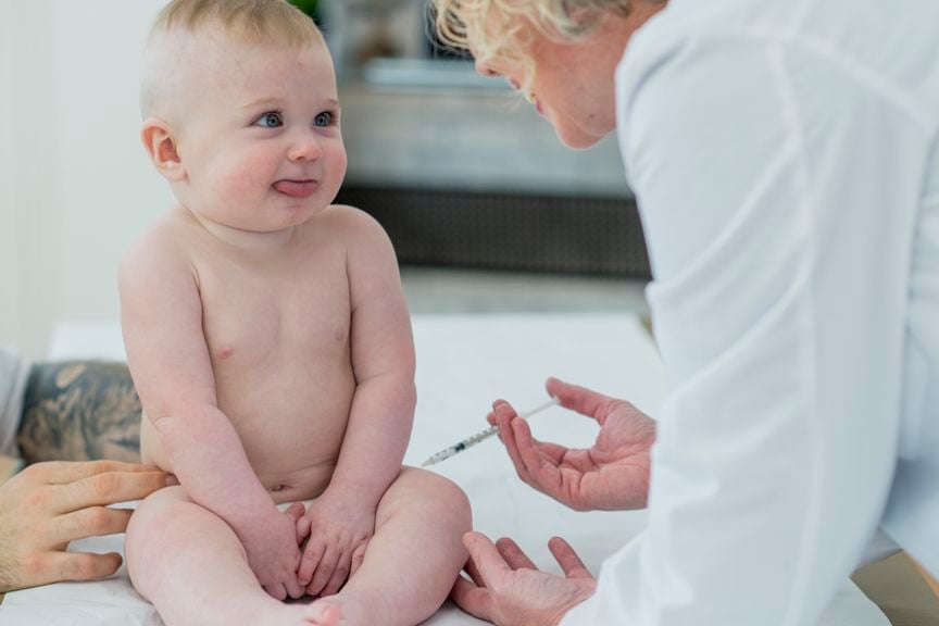 Skeptisch blickendes Kleinkind wird von einer Kinderärztin geimpft