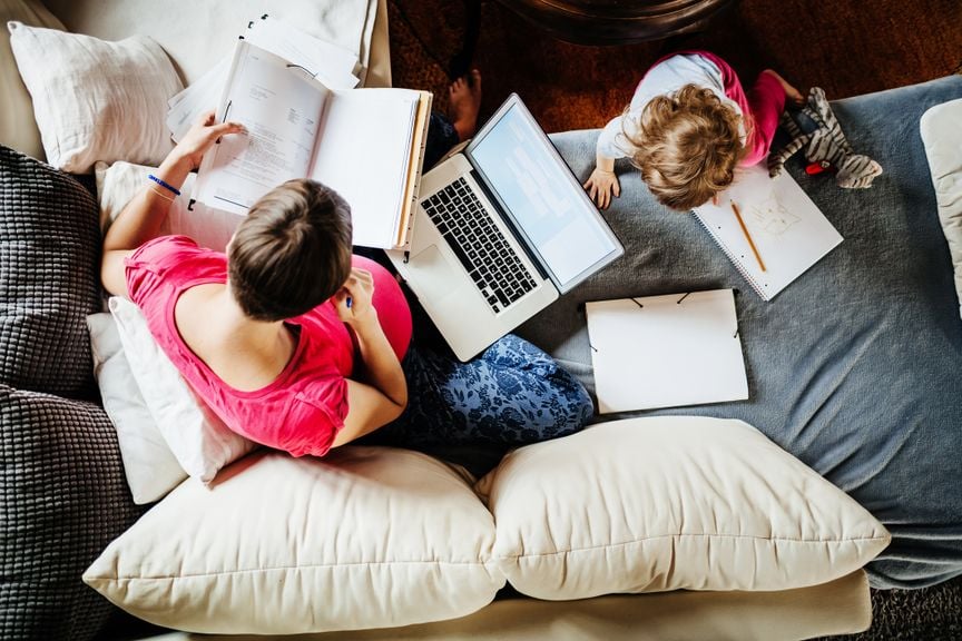 Schwangere Mutter mit dem Laptop, Kind klettert auf Sofa