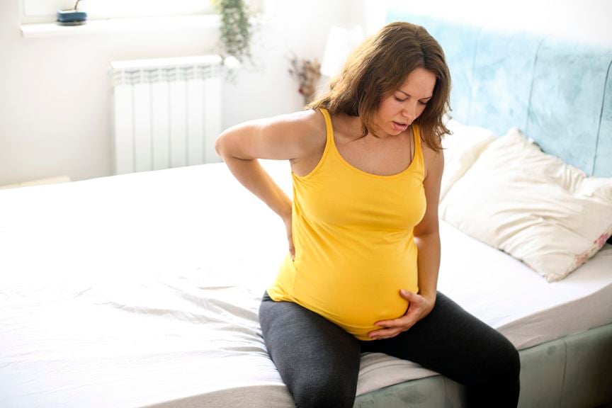 Hochschwangere Frau sitzt mit Rückenschmerzen oder Wehen auf dem Bettrand