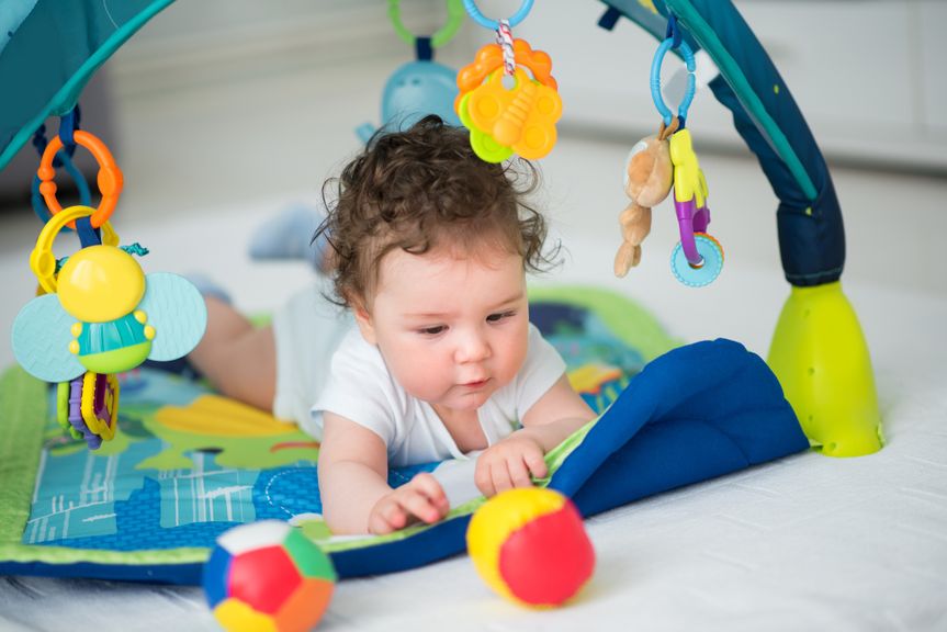 Baby umgeben von Spielbogen und buntem Spielzeug