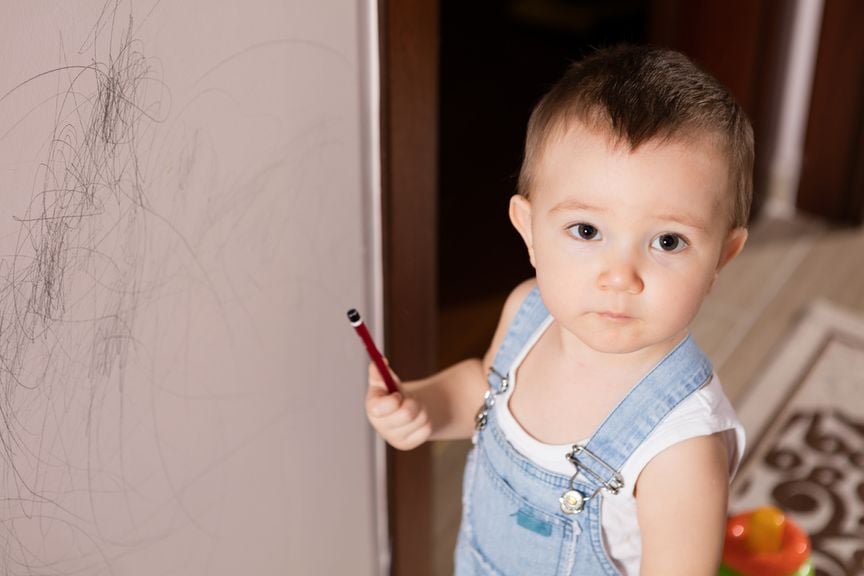 Verschämter Junge mit Stift vor angemalter Wand