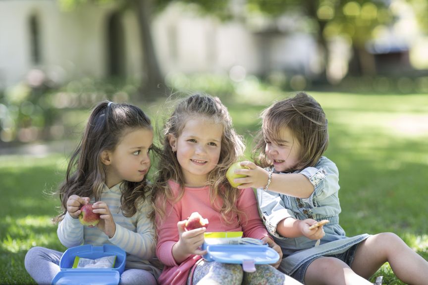 Mädchen sitzen auf dem Rasen und essen Snack