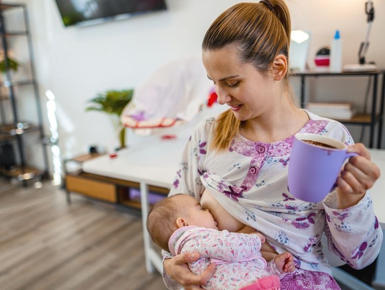 Mutter trinkt aus einer Tasse während sie ihr Baby stillt