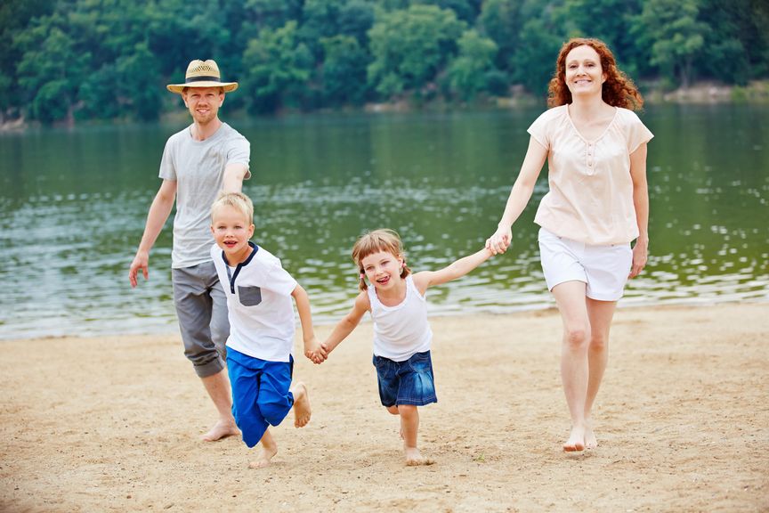 Familienferien am Strand; Eltern und zwei Kleinkinder gehen spazieren am sandigen Seeufer