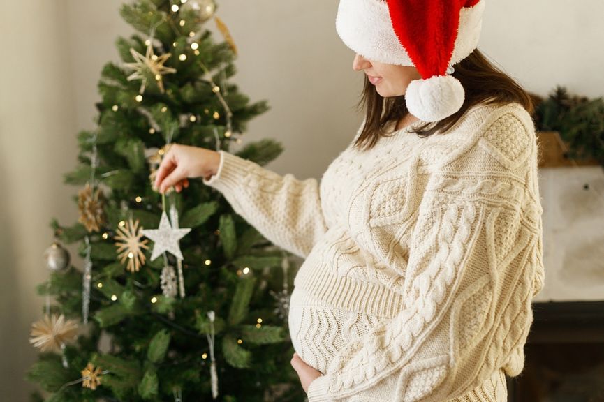 Schwangere Frau vor Weihnachtsbaum mit Sternanhänger in der Hand
