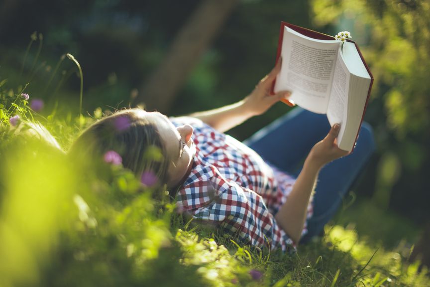 Frau liegt im Gras und liest in einem Buch