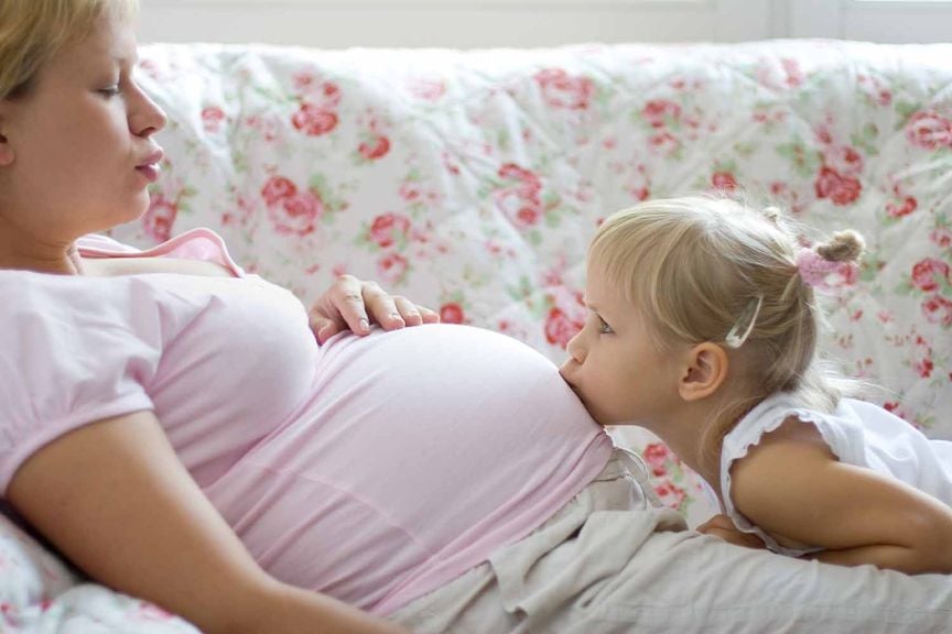 Mädchen küsst den Bauch der Mutter