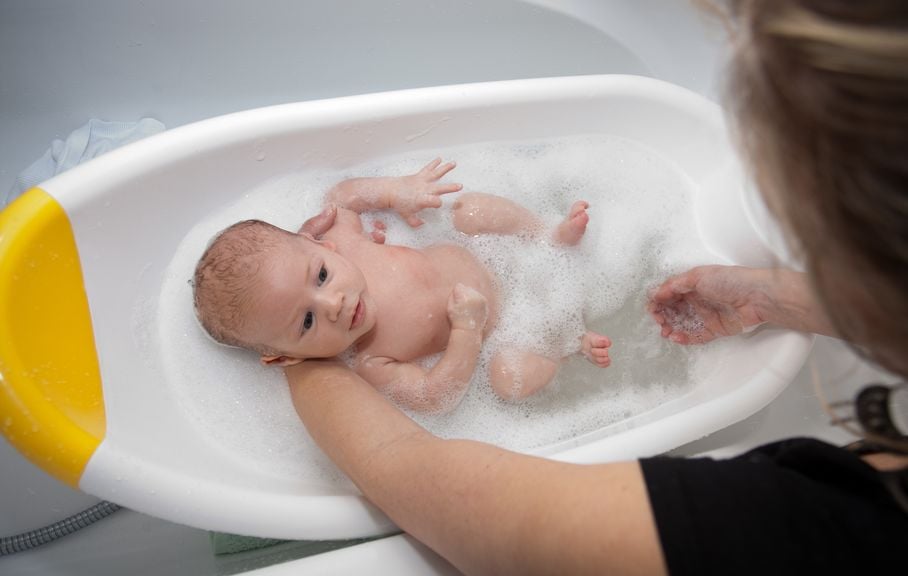 Mutter badet Neugeborenes in der Babybadewanne