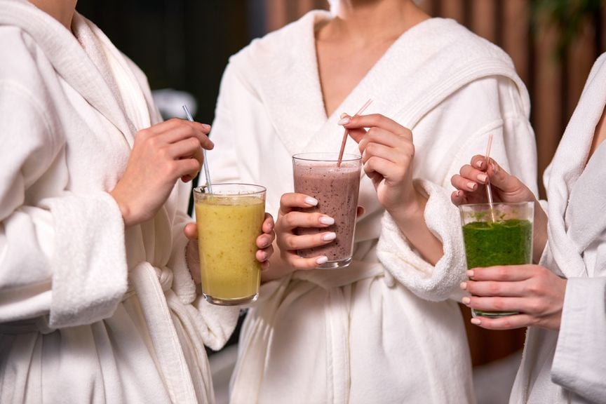 Drei Frauen in weissen Bademänteln mit Smoothies im Glas