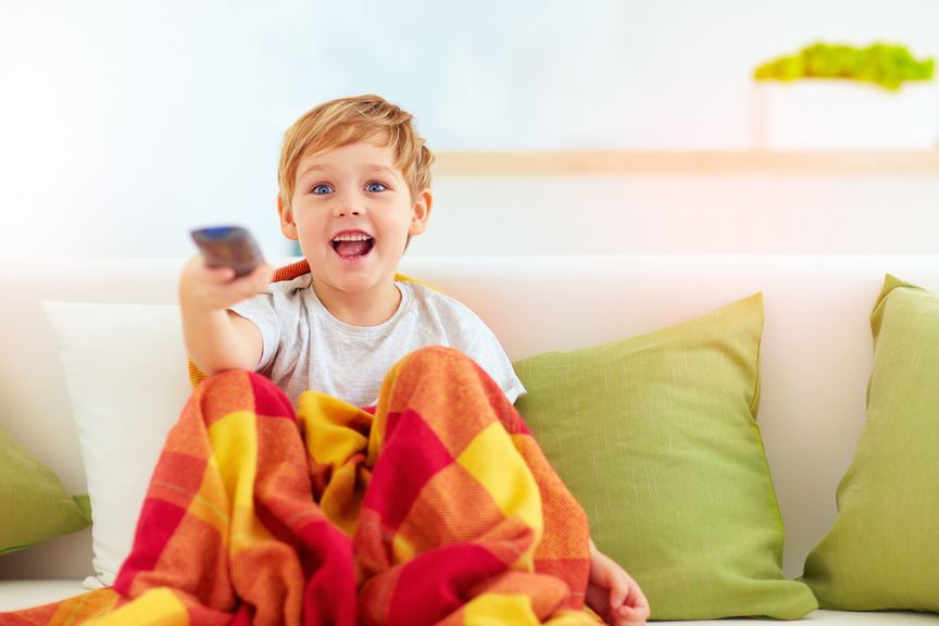 Lachendes Kind sitzt mit Fernbedienung in der Hand auf dem Sofa