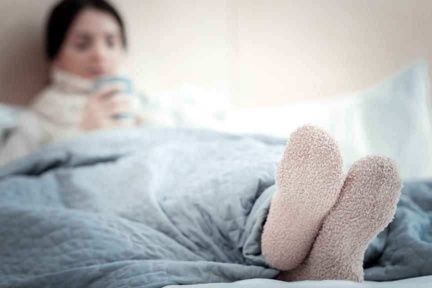 Frau im Bett mit Tee und warmen Socken