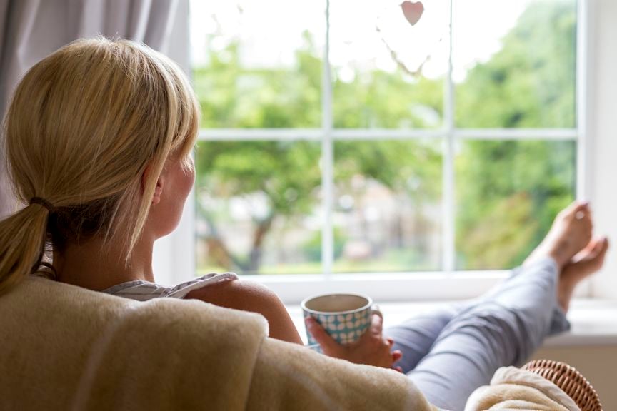 Frau sitzt vor dem Fenster, Beine hoch, mit Becher