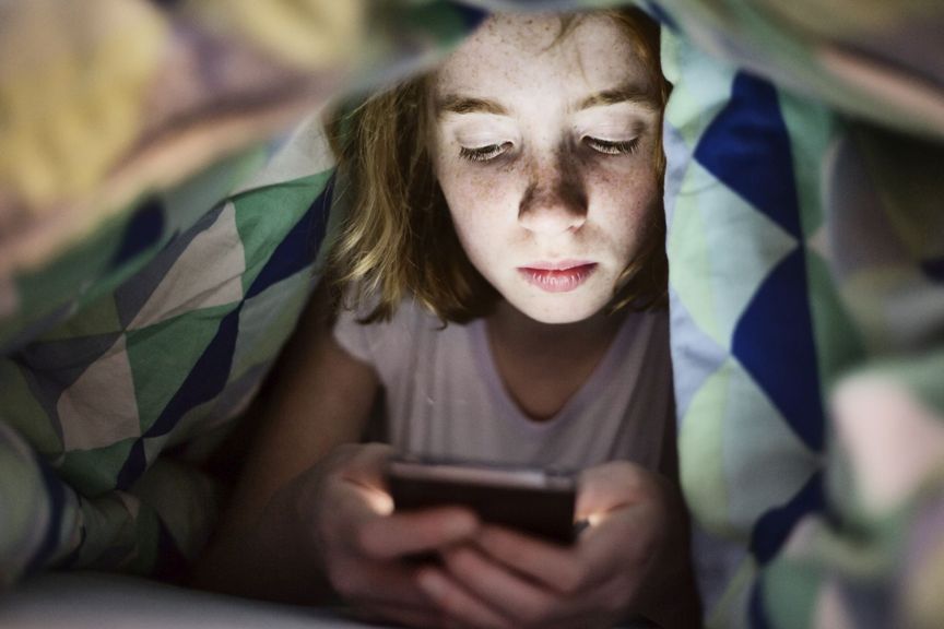 Kind mit Smartphone im Bett