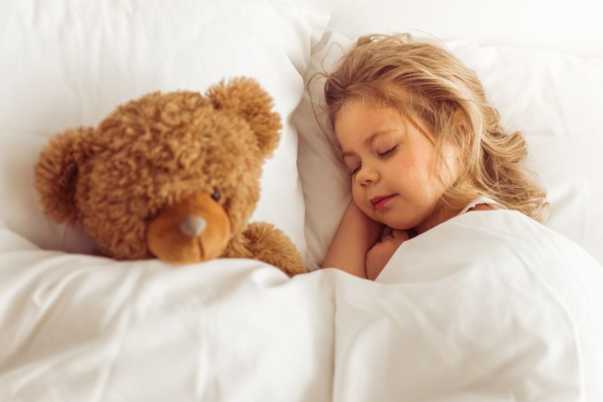 Mädchen schläft mit ihrem Teddy im Bett