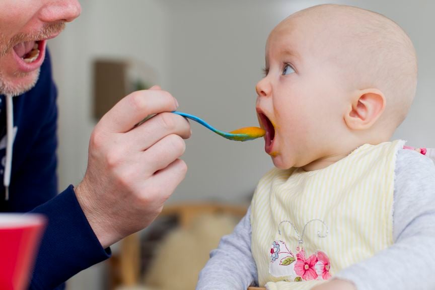 Baby wird von Vater mit Brei gefüttert