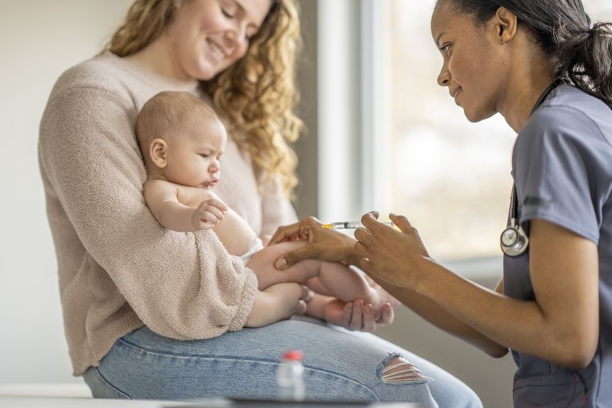 Baby sitzt auf dem Schoss der Mutter und bekommt eine Impfung verabreicht