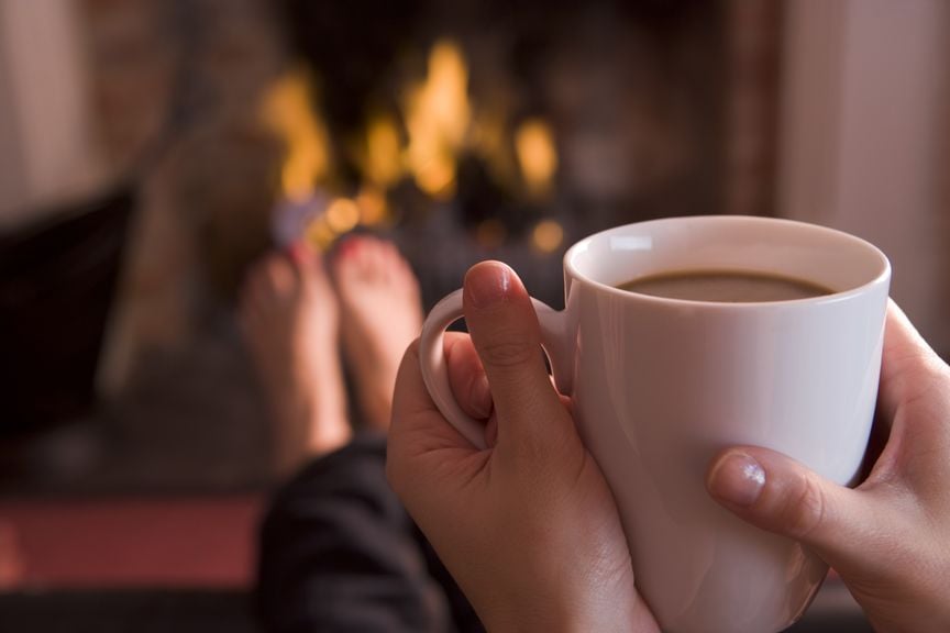 Tasse mit warmem Getränk in der Hand am Cheminée