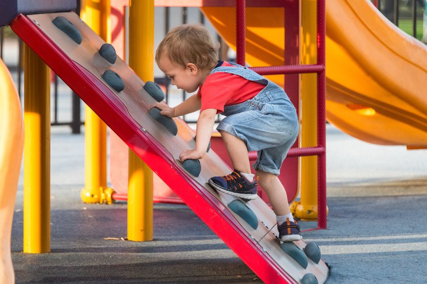 Kleiner Junge klettert auf ein Spielgerät auf dem Spielplatz