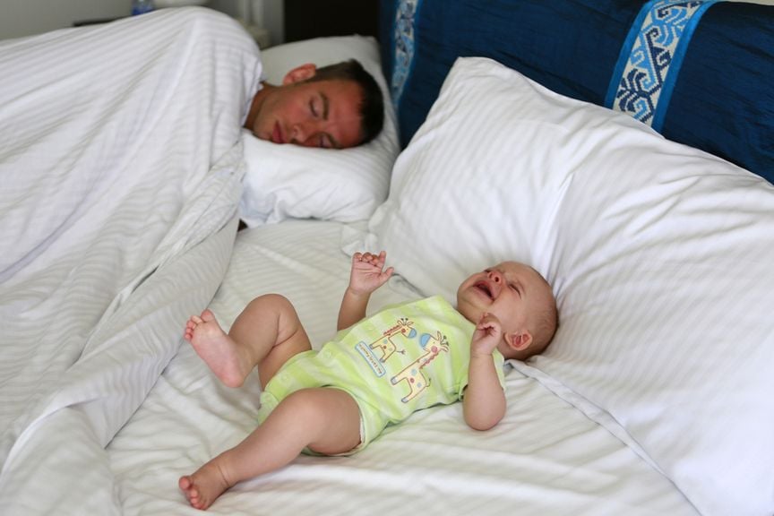 Mann schläft neben einem weinenden Baby