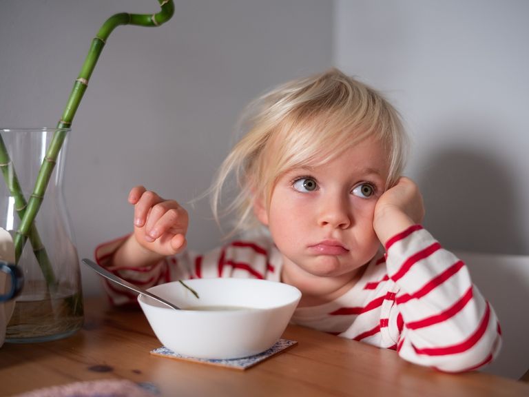 Kind mit aufgestütztem Kopf sitzt lustlos vor einem Teller mit Suppe
