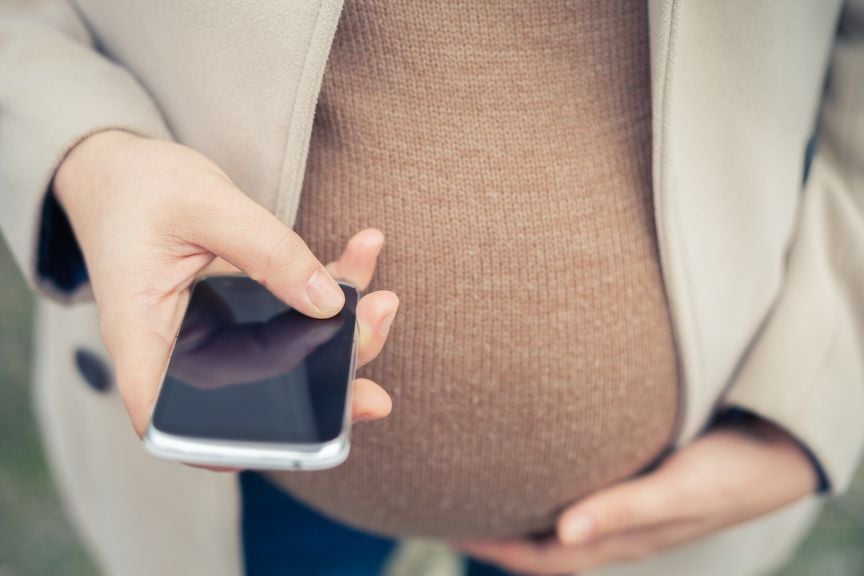 Schwangere hält sich den Bauch, Handy in der Hand