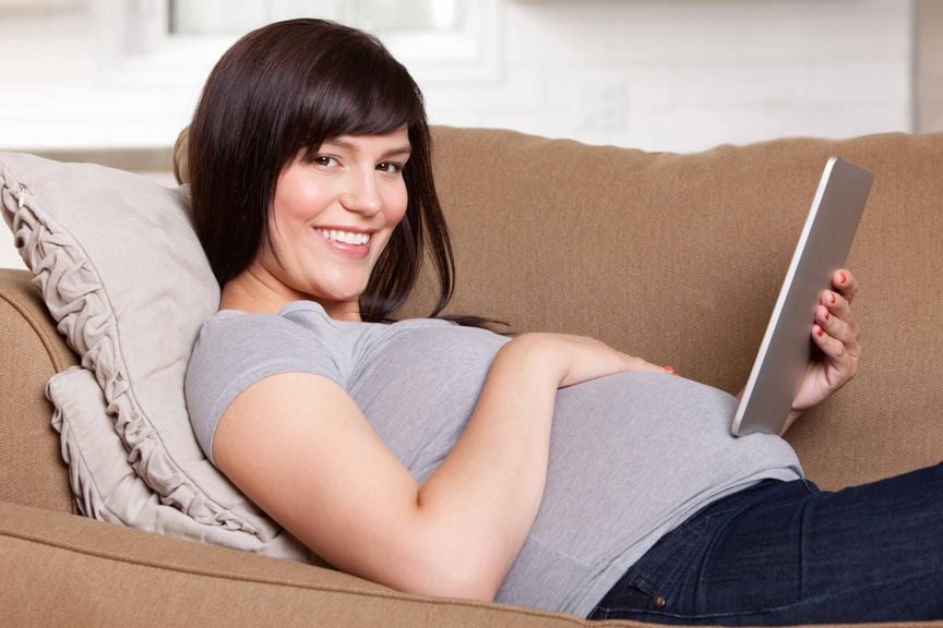 Schwangere liegt auf dem Sofa mit Tablet