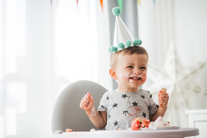 Baby mit Partyhut und verschmierten Händen und Mund