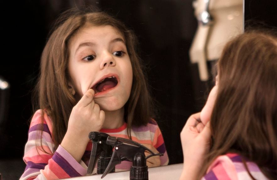 Mädchen schaut sich die Zähne im Spiegel an