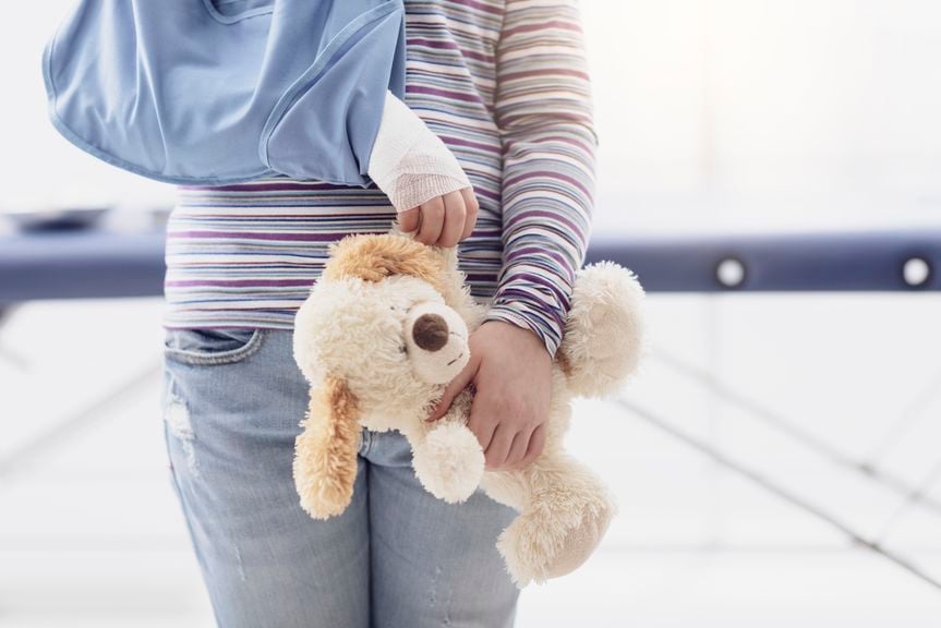 Kind mit Arm in der Schlinge und Teddybär