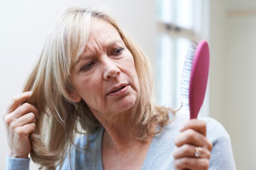 Frau schaut stirnrunzelnd die Haarbürste an