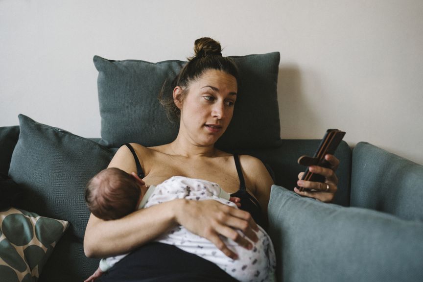 Mutter mit Handy stillt ihr Baby auf dem Sofa