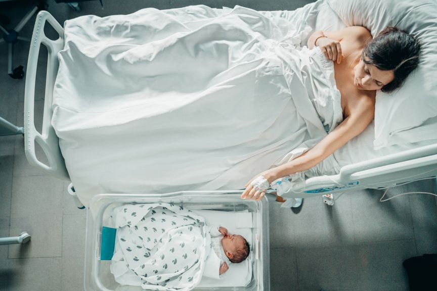 Mutter im Spitalbett betrachtet ihr Baby