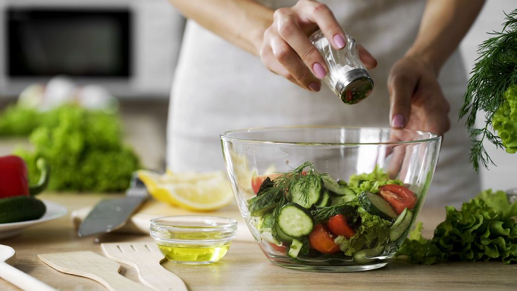 Frau streut Salz auf Gemüse in einer Salatschüssel
