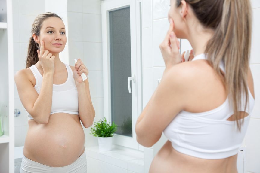 Schwangere cremt sich vor dem Spiegel das Gesicht ein