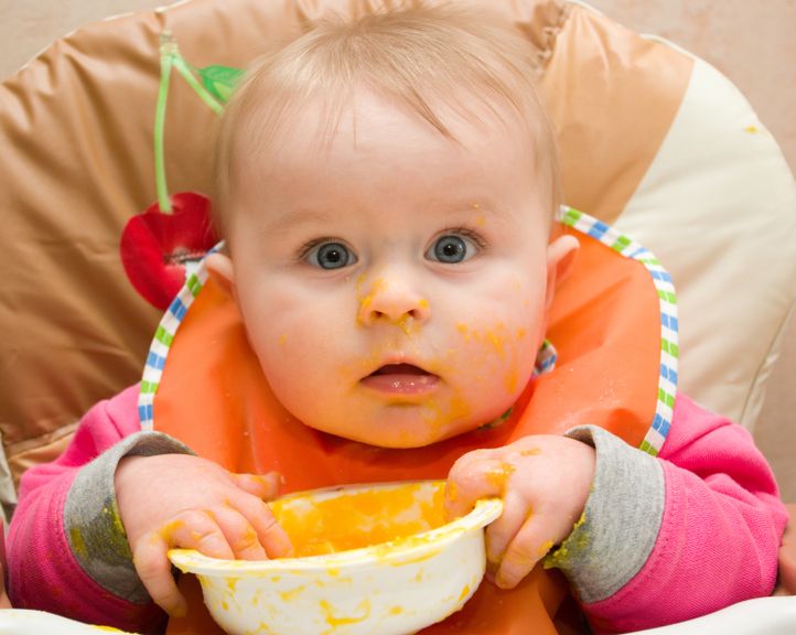 Baby mit Breischüssel und Latz isst mit den Fingern