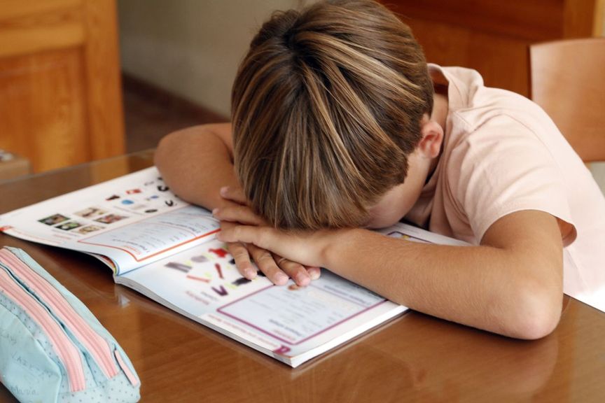 Schulkind liegt mit dem Kopf auf einem Schulbuch