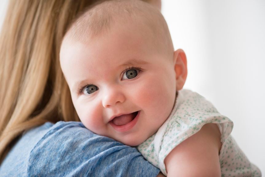 Baby lächelt an Mamas Schulter