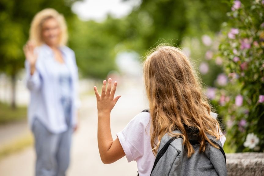Mutter winkt ihrem Schulkind zum Abschied