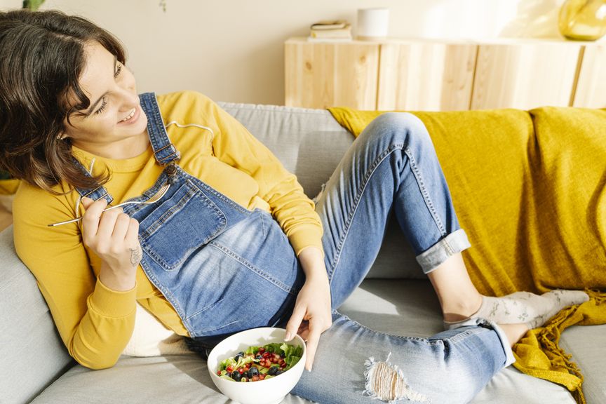 Schwangere auf dem Sofa mit einer Salatschüssel